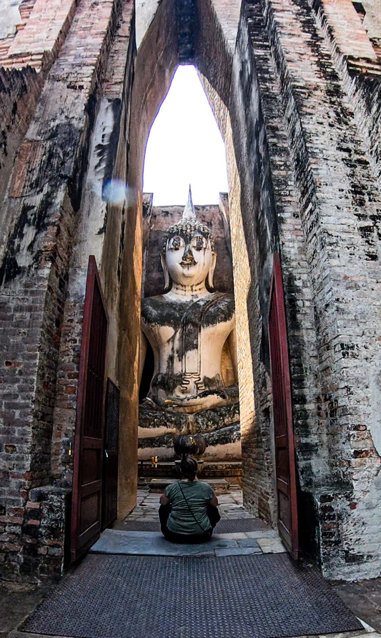 Voyageuse assise face à une immense statue de Bouddha dans un temple ancien de Sukhothaï, Thaïlande