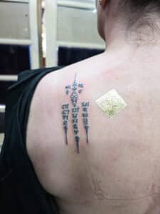 Tatouage sacré Sak Yant fraîchement réalisé sur l’omoplate, orné d’une feuille d’or symbolisant la bénédiction du moine.