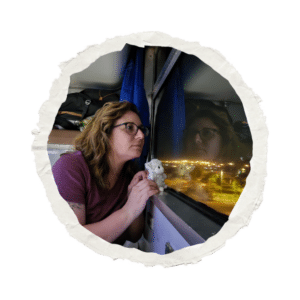 Voyageuse regardant par la fenêtre d’un train de nuit, tenant une petite peluche dans les mains, reflet lumineux sur la vitre.