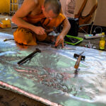 Un moine bouddhiste utilisant des outils traditionnels pour ciseler une plaque d'argent au temple Wat Sri Suphan.