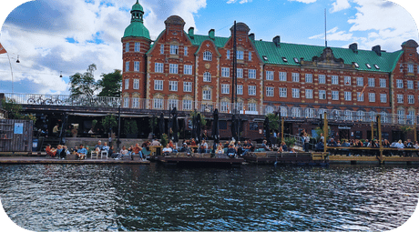 Façade historique en briques rouges aux toits verts bordant un canal animé à Copenhague, avec terrasses et bateaux