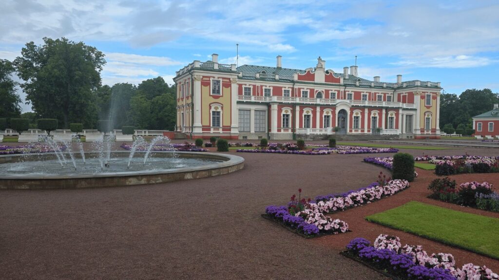 Façade baroque rouge et jaune du palais de Kadriorg avec fontaine en jets d'eau et parterres de fleurs violettes et roses en premier plan
