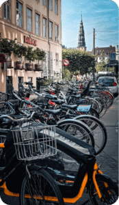 Rangée de vélos garés dans une rue pavée du centre historique, avec clocher en arrière-plan à Copenhague